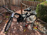 Overall view of green Mountain Track bike leaning on patio with leaves, helmet hanging from handlebars and pump at rear wheel