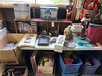 Overview of table under window showing SNES, N64 consoles with cartridges, boxed PlayStation DualShock, Skylanders set, shelf of game discs, and Christmas figurines