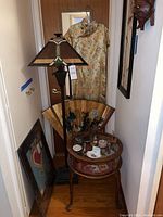 Overall view of lot showing table with contents, lamp, fan, dress, framed art and mask