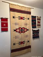 Photo showing the set of 5 Southwestern woven rugs hung on a wall with visible fringed edges and geometric patterns in traditional Southwestern colors of red, blue, beige, black.