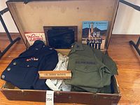 Photo showing vintage U.S. Air Force uniforms, wooden plaque, nameplate inside an old trunk with packed materials.
