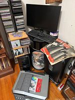Photo of computer monitor, wireless keyboard and mouse, stacks of CDs, a printer, vintage LIFE magazines, and a globe on a wooden floor.