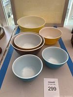 Photo showing six vintage Pyrex mixing bowls in yellow, white, brown with floral design, and blue colors, arranged on a surface for display.