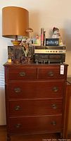 Front view of the wooden dresser with items on top including lamp, electronics, clown and snowman figurines, and books