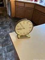 Brass Art Deco clock from 1950s displayed on kitchen counter showing front and base.