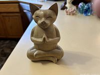 Front view of carved wooden cat figurine in yoga pose showing detailed face and hands pressed together.