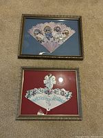 Both framed fans shown together, one on blue background and one on red background, placed on carpeted floor.