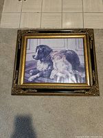 Framed artwork depicting a little girl resting with a large dog, in a decorative gold and black frame.