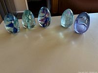 Front view of five glass eggs arranged side by side showing different internal designs and colors.