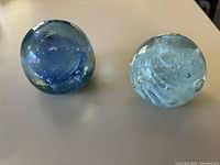 Two round glass ornaments on a flat surface, showing dark blue and light blue ash inclusions.
