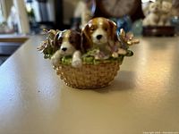 Front close-up of the trinket keeper showing two puppies inside a woven basket with floral decorations.