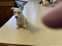 Front side view of a white porcelain terrier dog figurine with black-painted eyes and nose, showing detailed craftsmanship and glossy finish.