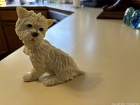 Photo of a white Westie dog figurine in sitting pose with textured fur detail and realistic black eyes and nose, on a kitchen counter.