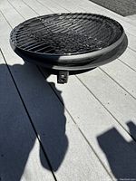 Top view of the metal fire pit with a round shape and mesh grill placed on wooden outdoor deck.