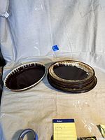 Photo of 10 vintage Pfaltzgraff Gourmet Brown Drip large platters in two stacks on a cloth surface, showing brown drip glaze pattern with cream edges.