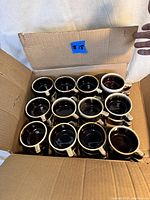 Top-down view of 12 vintage Pfaltzgraff coffee cups neatly arranged in a cardboard box.