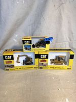 Three CAT diecast construction vehicle models in original boxes displayed side by side: Cat 906 Compact Wheel Loader, Cat 308C CR Hydraulic Excavator, Cat D6N XL Track Type Tractor