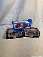 Three boxed vintage fire department diecast vehicles arranged together, two Gearbox Toys SUVs and one Siku ladder truck, all red and in 1:43 scale.