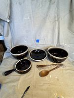 Four brown drip bowls displayed together with two wooden spoons on a beige cloth background.