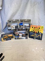 Five diecast vehicle models in original packaging displayed on a surface, showing brands CAT, CASE, VOLVO, and ERTL.
