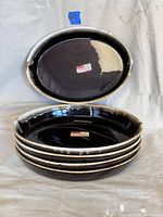 Stacked view of five large oval ceramic platters with brown drip glaze around the edge.