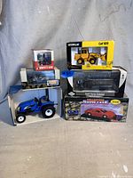 Photo showing the six boxed vintage diecast vehicles including Caterpillar loader, Ford truck, blue tractor, and a collector's show case.
