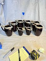 Eight ceramic brown drip pitchers arranged in two rows, showing size variation and drip glaze.