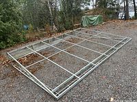 Photo showing large rectangular aluminum frame on gravel, viewed from side angle with visible crossbars