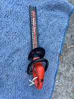Full view of the Black & Decker Hedge Hog electric hedge trimmer laid on a blue fabric surface showing the entire length with blade and handle.