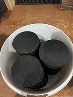 Top view of a white bucket filled with multiple black hockey pucks stacked inside.