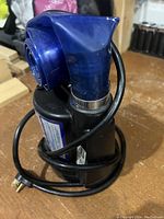 Close-up side view showing the blue coiled hose attached to the black pump and the power cord plug.