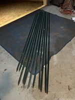 View of nine green steel T-posts approximately 8 feet long laid on floor, showing pointed ends.