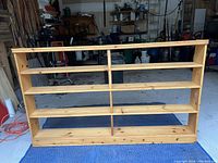 Front view of wooden shelving unit showing four shelves and wood grain with marks.