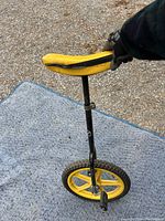 Photo of a yellow and black unicycle showing padded foam seat and single wheel with pedals on outdoor surface.