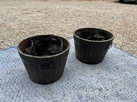 Front angle of two black wooden barrel planters on a blue tarp outdoors, showing plastic liners inside each barrel.