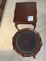 Two wood accent tables, one round with black top and gold border, one square with scalloped edges.