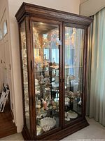 Front view of the brown wood curio cabinet showing glass doors, wood grain finish, and visible items inside (not included).
