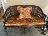 Full front view of wicker love seat with floral cushions and ruffle pillow on top