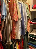 Men's tops hung on hangers, showing various plaid, checkered, and solid color dress and casual shirts.