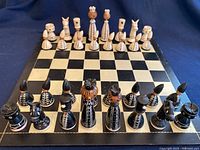 Full view of the chess board with all white and black chess pieces arranged facing each other in starting positions, showcasing hand carved and painted details.