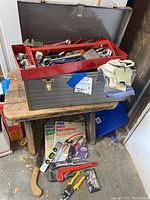 Open metal Craftsman toolbox with red top tray filled with various hand tools and gloves resting on the side. Toolbox is dented and rusty.