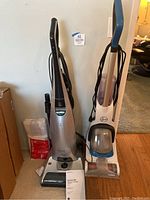 Both the Hoover steam cleaner in white and blue and the Kenmore Elite vacuum cleaner with silver body standing side by side.