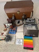 Full overview of lot showing brown leather camera carrying case, Kodak Pony 135 camera with brown leather case, Polaroid Land Camera Automatic 230, boxes of flashbulbs, color film box, flashcubes, camera manual, and other paperwork.