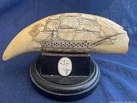Front view of faux scrimshaw whale tooth showing detailed ship engraving and base with engraved plaque.
