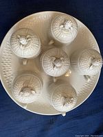 Top view of 6 ceramic pots de crème with lids on underplate, showing uniform seed pattern and finials on lids