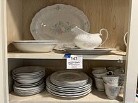 Porcelain plates, bowls, cups, gravy boat, and serving tray arranged on shelves showing the full set.