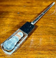 Letter opener lying on a wooden surface showing lucite handle with embedded Canadian coins from 1967 Centennial series.