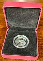 Closed red display box containing the silver coin in a protective plastic case on black velvet lining.