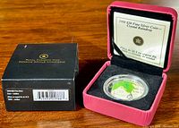 Outer black Royal Canadian Mint box with barcode next to pink display case containing coin