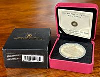 Photo of the coin in the red presentation box and original black outer box showing product label.
